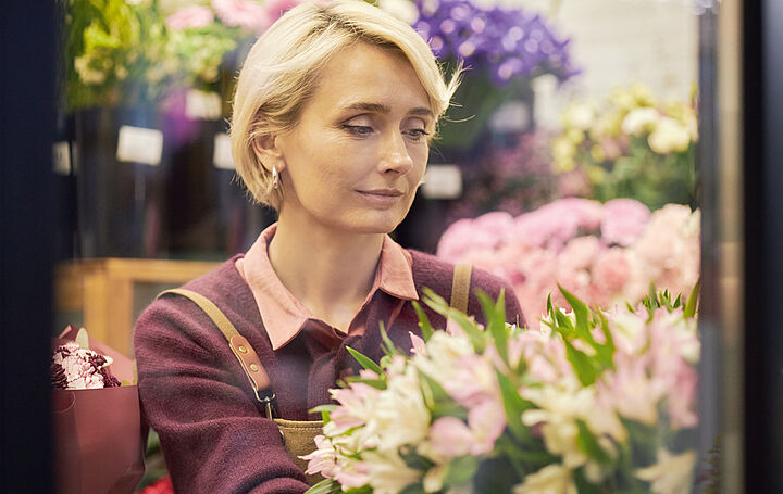 Eine blonde Frau in einem Blumengeschäft. Sie sieht traurig aus.