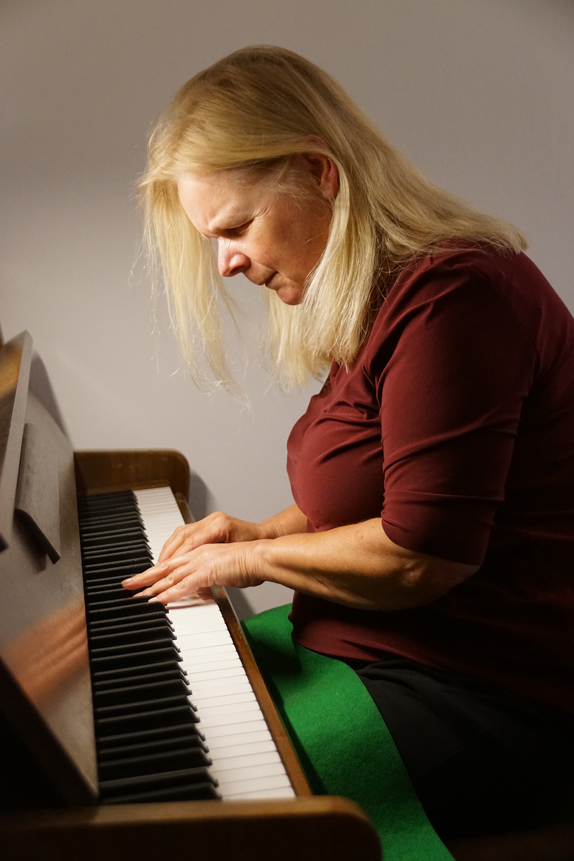 Eine Frau mit langen hellblonden Haaren sitzt vor einem Klavier und spielt konzentriert mit beiden Händen.